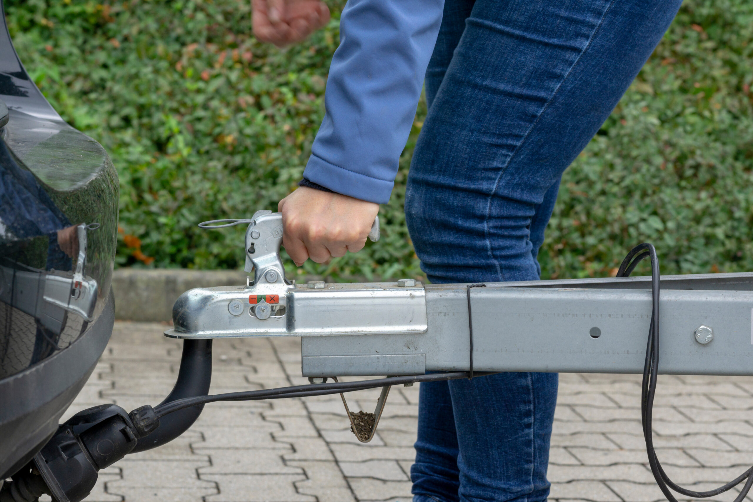 Person securing a rental trailer hitch to a vehicle, ensuring proper connection for safe towing.